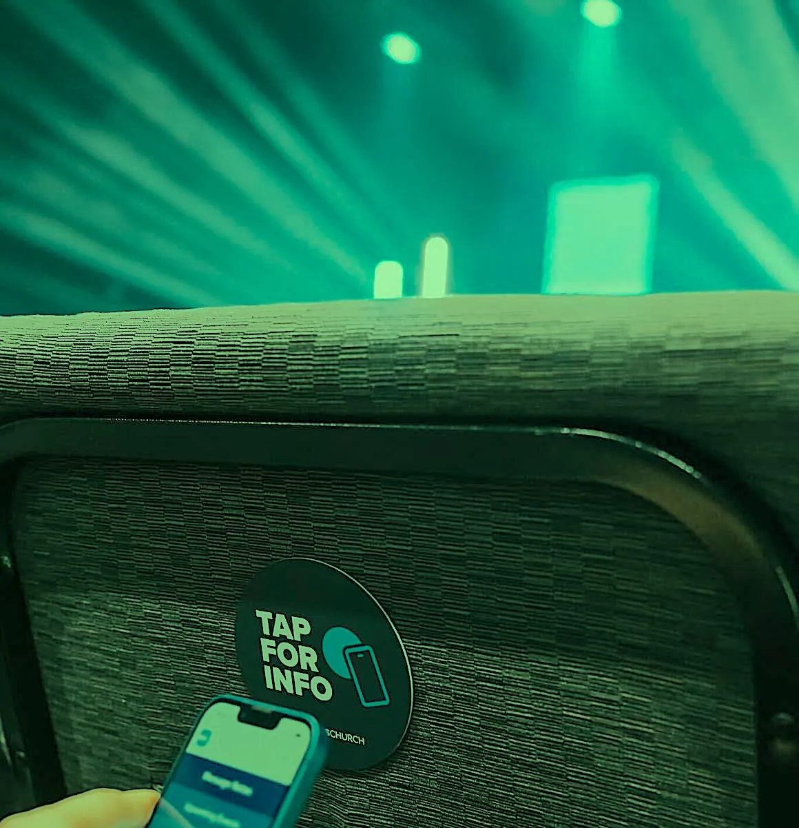 A phone tapping a round NFC tag on a church chair, labeled Tap for Info