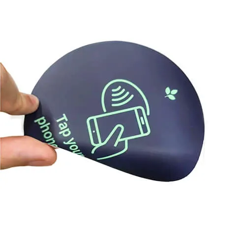 A hand holding a round NFC tag with a phone-tap symbol